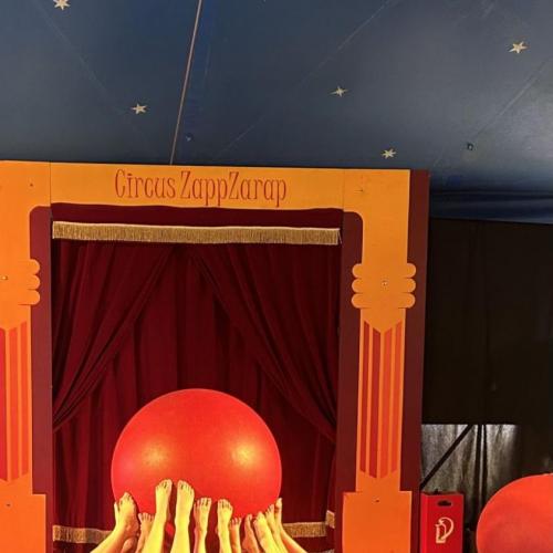 Im Zirkus ZapZarap wird ein großer roter Gymnastikball von vielen nackten Füßen in die Luft gehoben